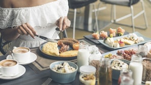 Une femme est assise à une table et prend son petit-déjeuner, qui comprend divers aliments, notamment des œufs, du bacon et des viennoiseries.