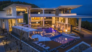 Une maison moderne à plusieurs étages, dotée d’une grande piscine extérieure, de nombreux balcons et d’un intérieur bien éclairé.