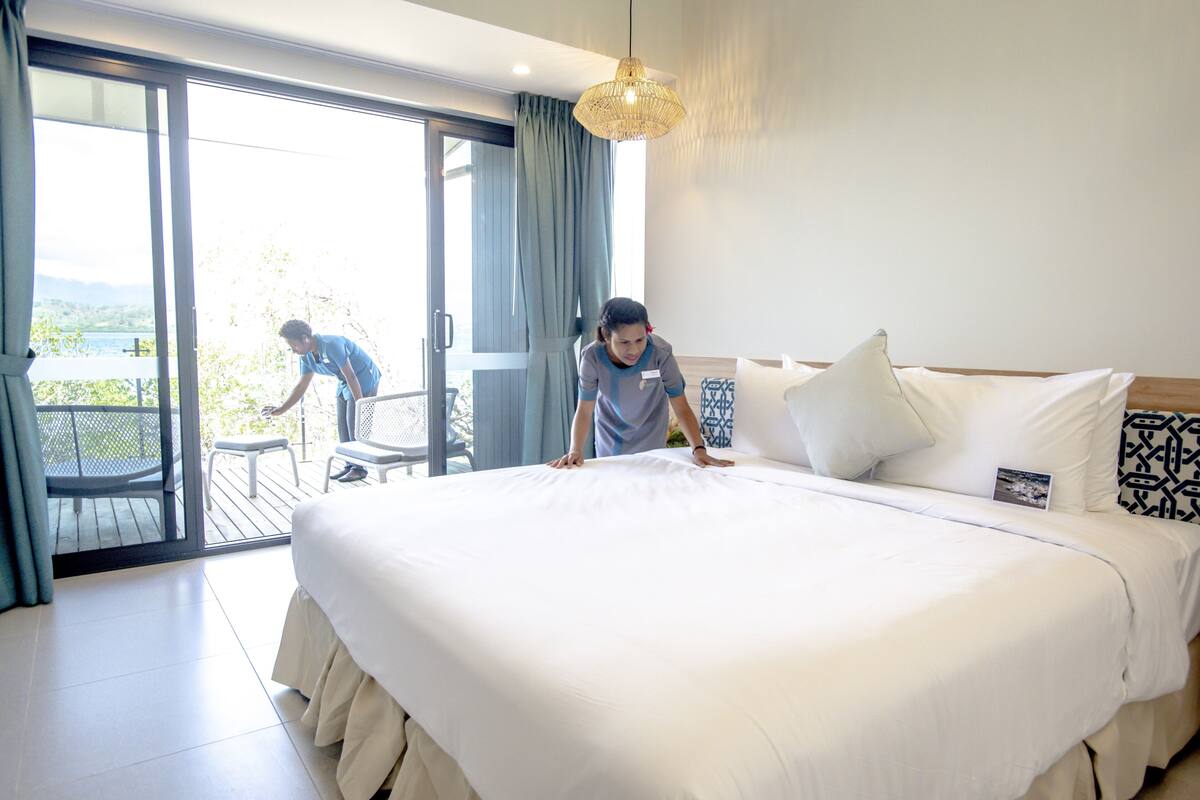 Une chambre d’hôtel avec un grand lit, un balcon doté d’une table et de chaises, et une vue sur l’extérieur.