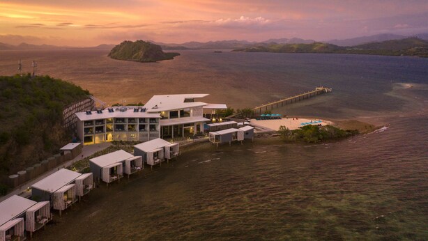 Un hôtel situé sur la côte, doté d’un design moderne, avec un grand bâtiment comprenant de nombreuses chambres et une longue jetée s’avançant dans l’eau.