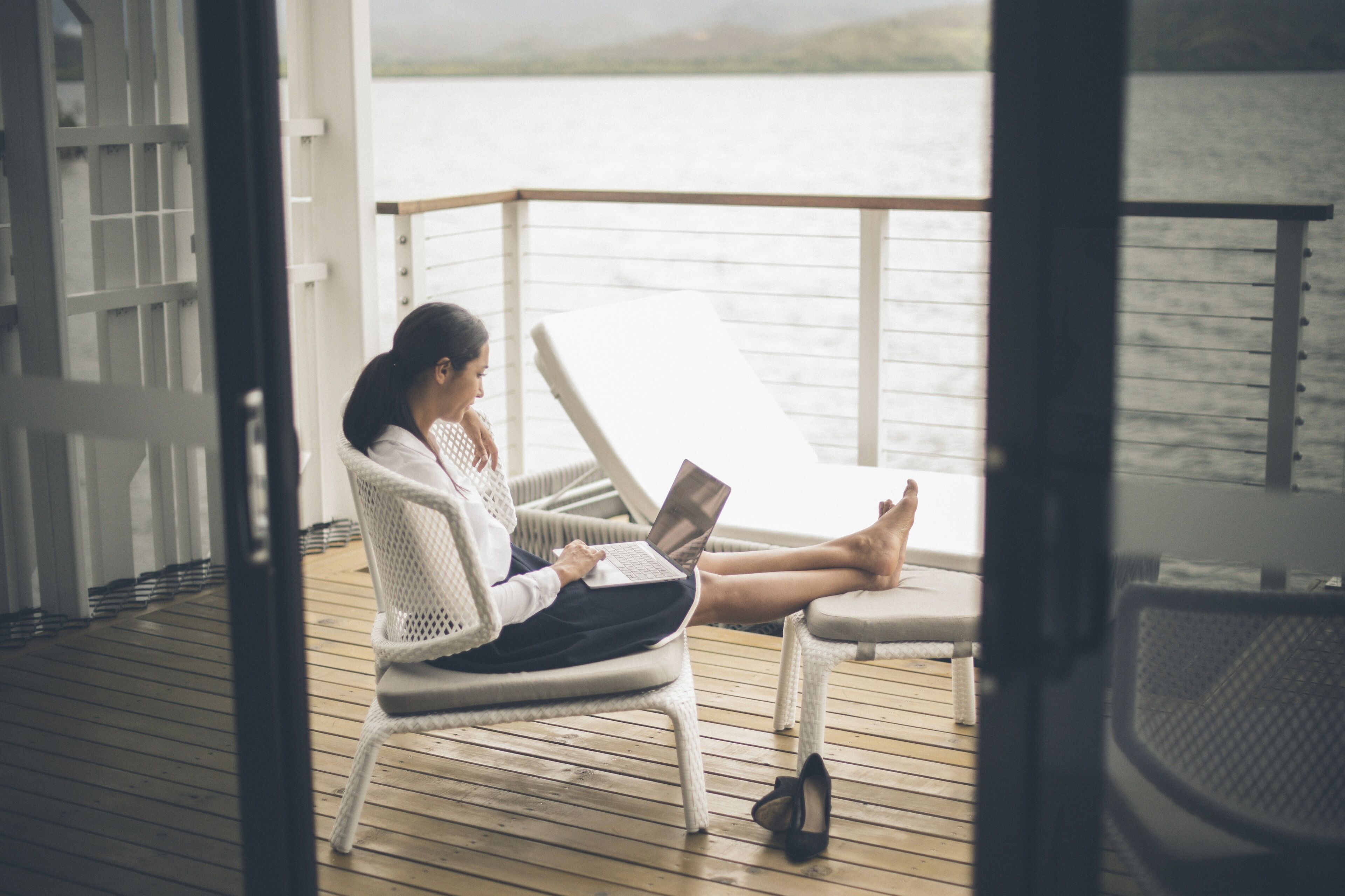 A person sitting on a wicker chair on a wooden deck, using a laptop.
