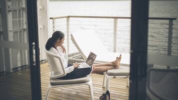 A person sitting on a wicker chair on a wooden deck, using a laptop.