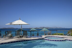 A pool area with lounge chairs and umbrellas, overlooking the sea.