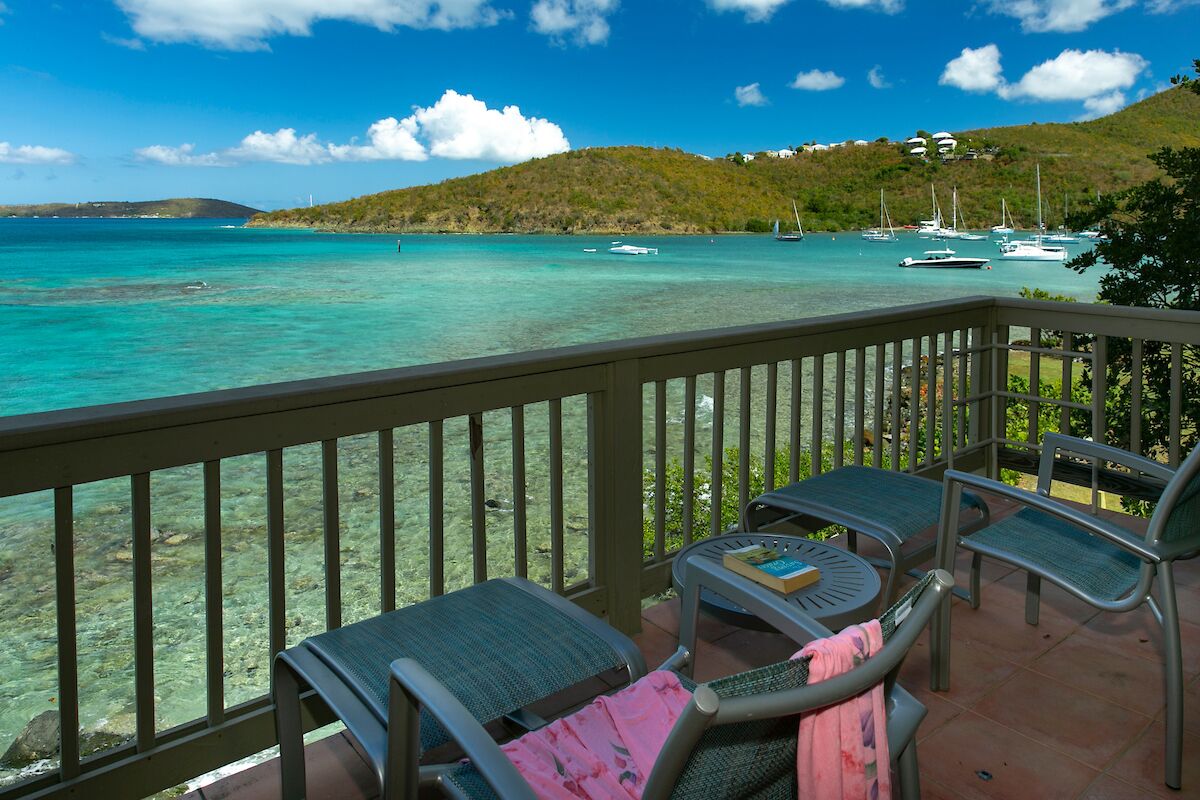 A balcony with a view of turquoise waters and boats, surrounded by greenery and hills.