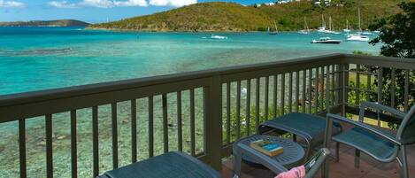 A balcony with a view of turquoise waters and boats, surrounded by greenery and hills.