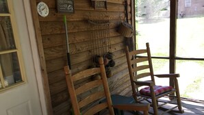 A wooden cabin interior with a rocking chair, a broom, and fishing equipment on the wall. - CREEKSIDE CABINS  - CHIPMUNK (Bryson City)