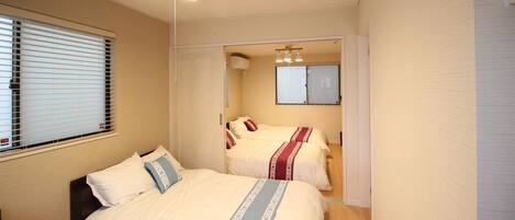 A bedroom with two beds, a ceiling fan, and a window with blinds.