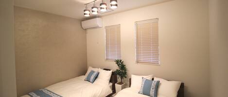A bedroom with two beds, a ceiling light fixture, and two windows with blinds.