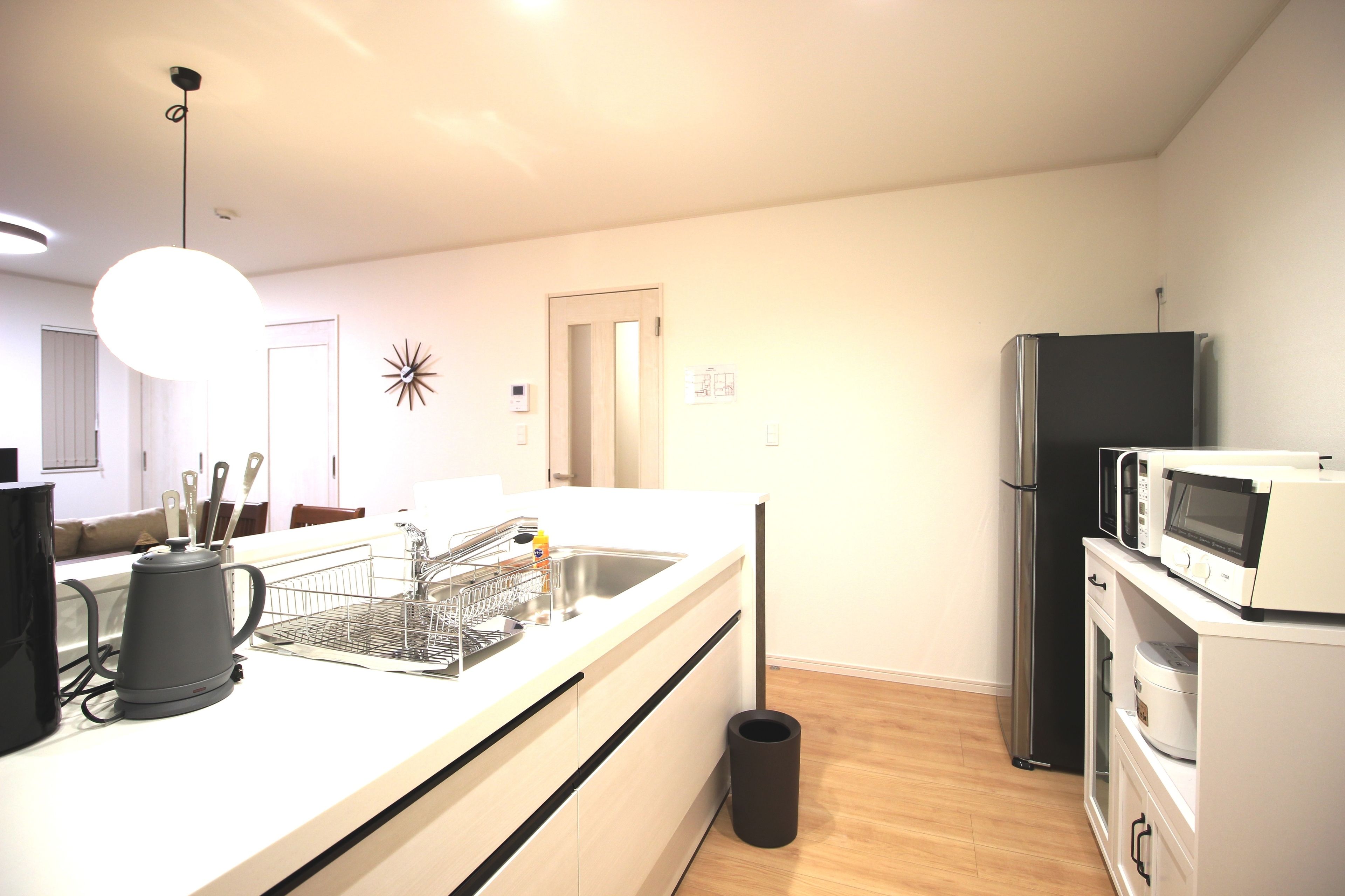 A modern kitchen with a white countertop, stainless steel sink, and a black trash can.