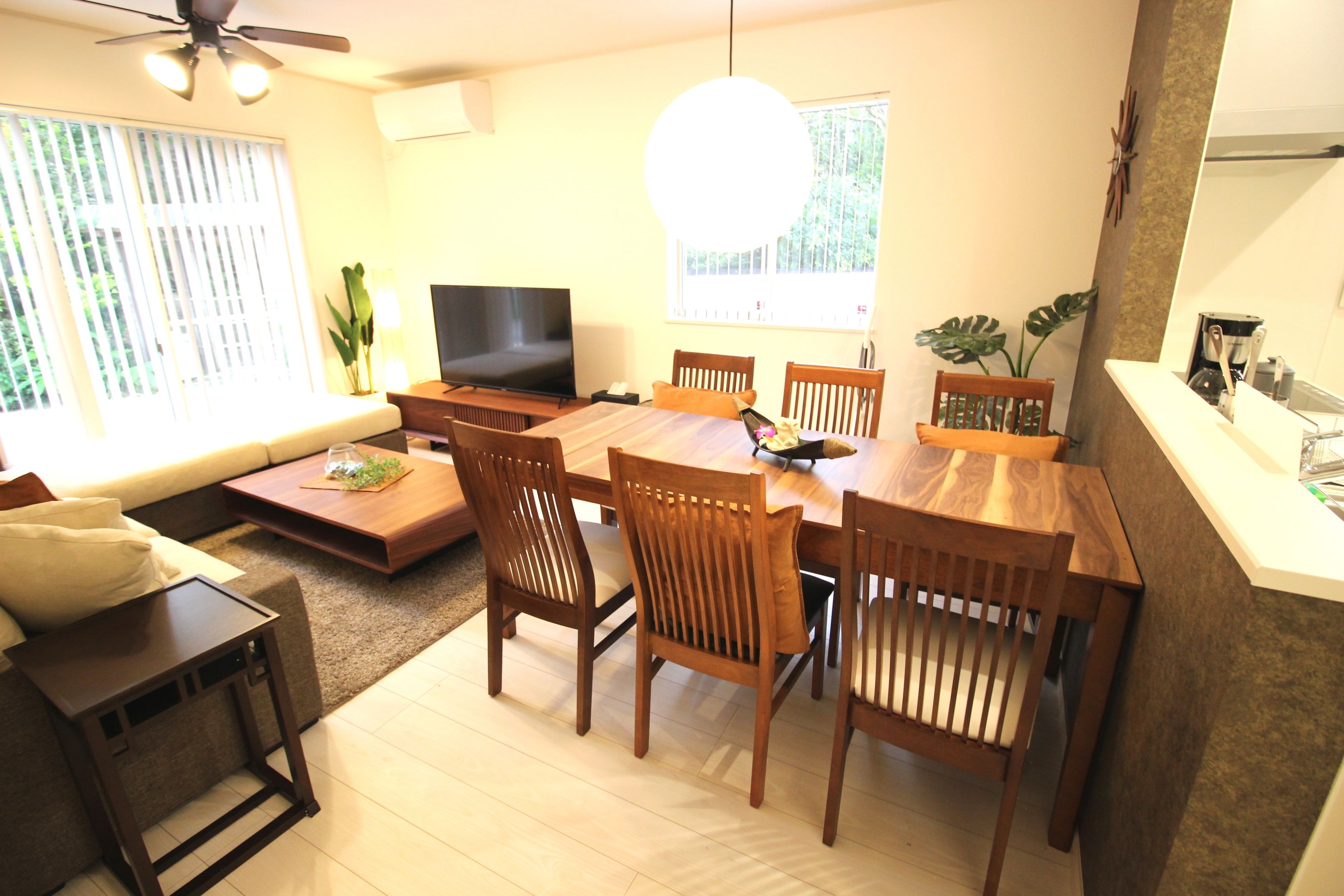 A dining area with a wooden table and chairs, a television, and a large window with blinds.