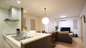 A modern kitchen with a central island, a dining area with chairs, a sofa, and a TV. - Hope Villa Onnason (Onna)