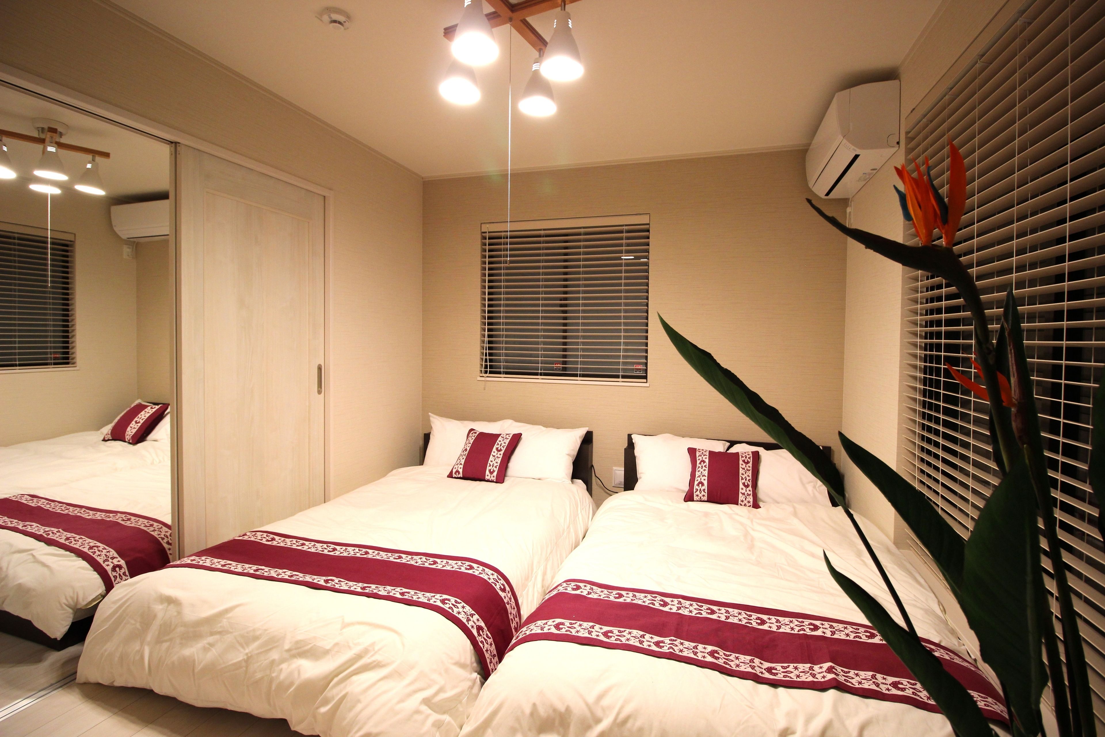 A bedroom with two beds, a large mirror, and a window with blinds.
