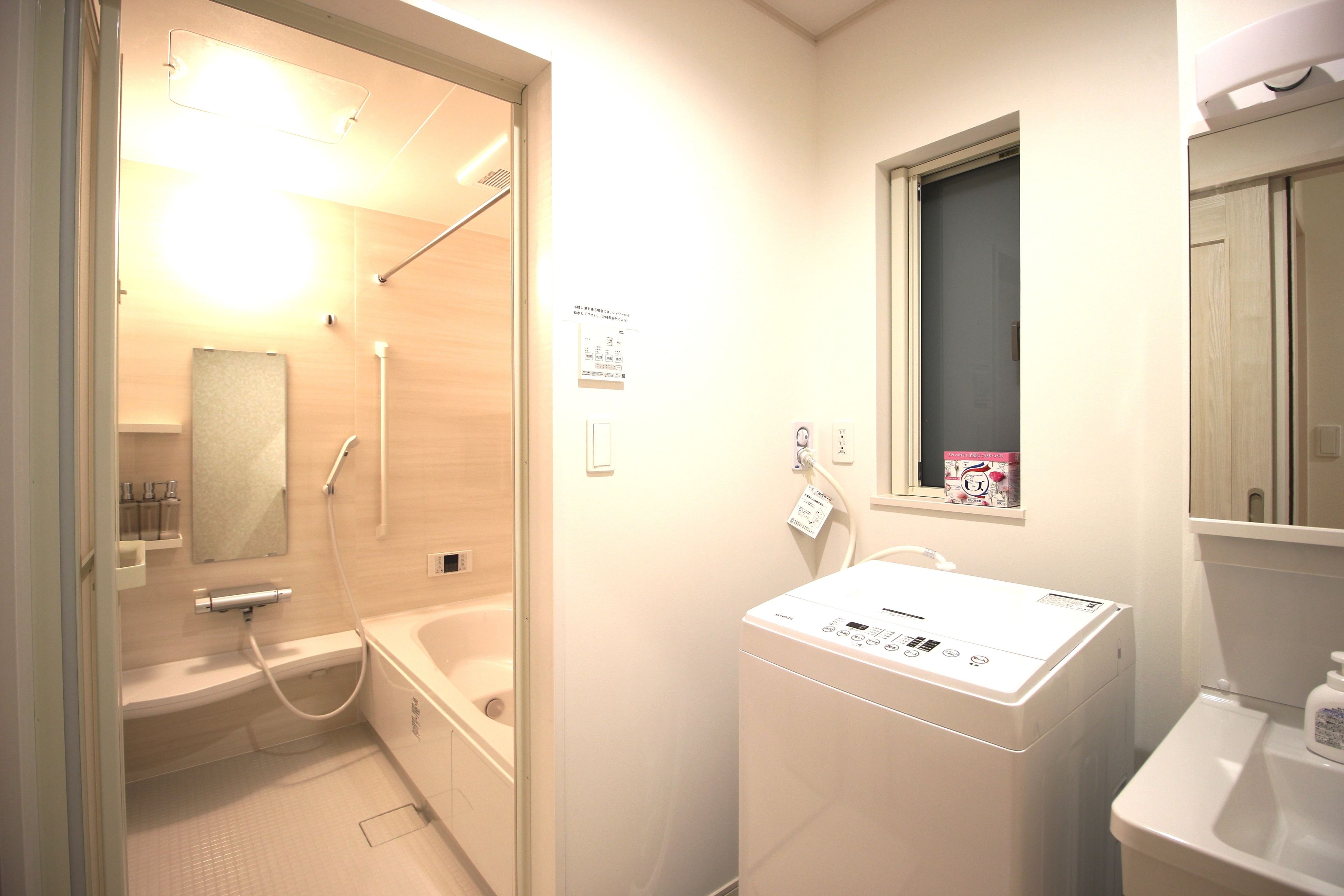 A bathroom with a bathtub, a washing machine, and a window.