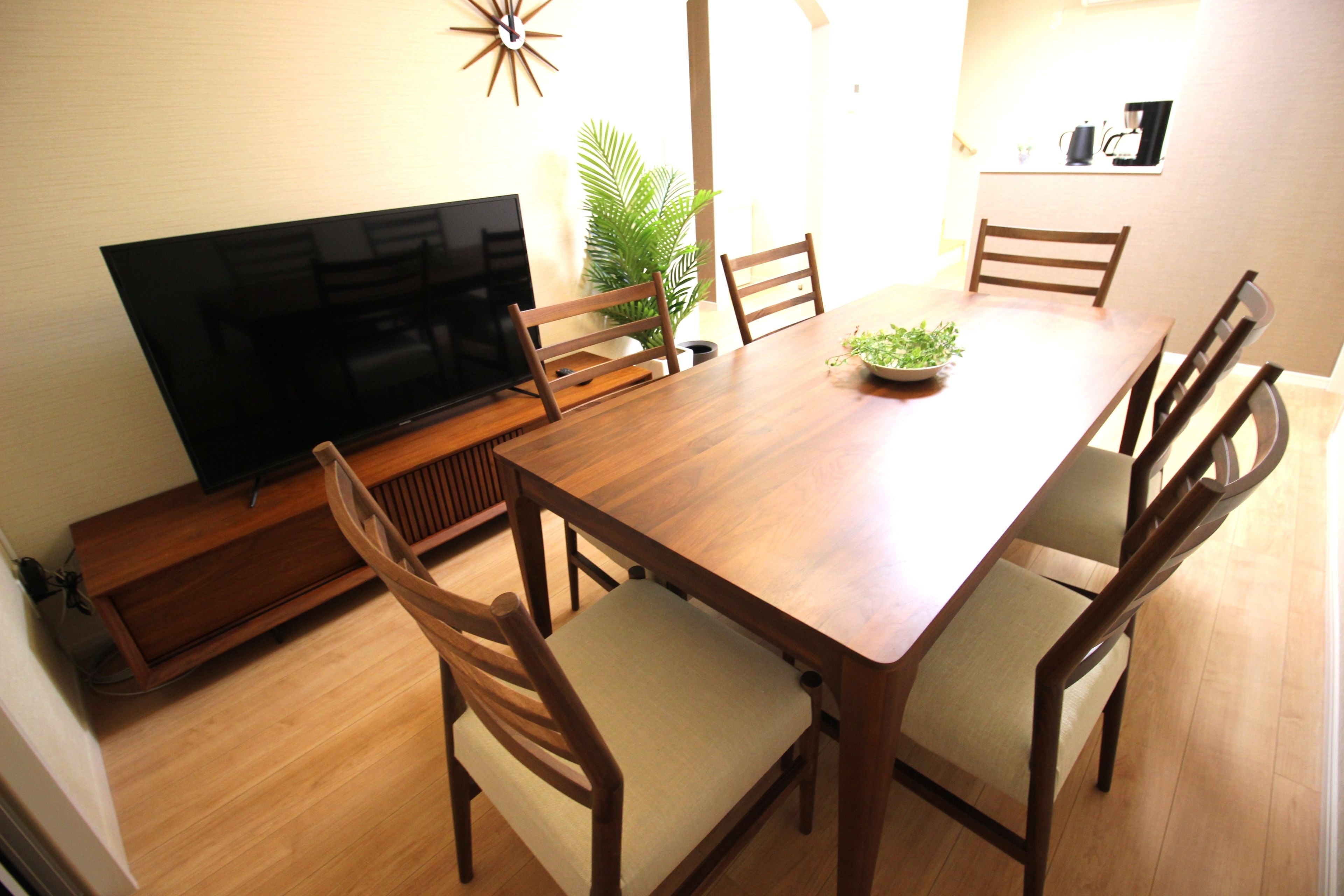 A dining area with a wooden table, six chairs, a television, a plant, and a coffee machine.