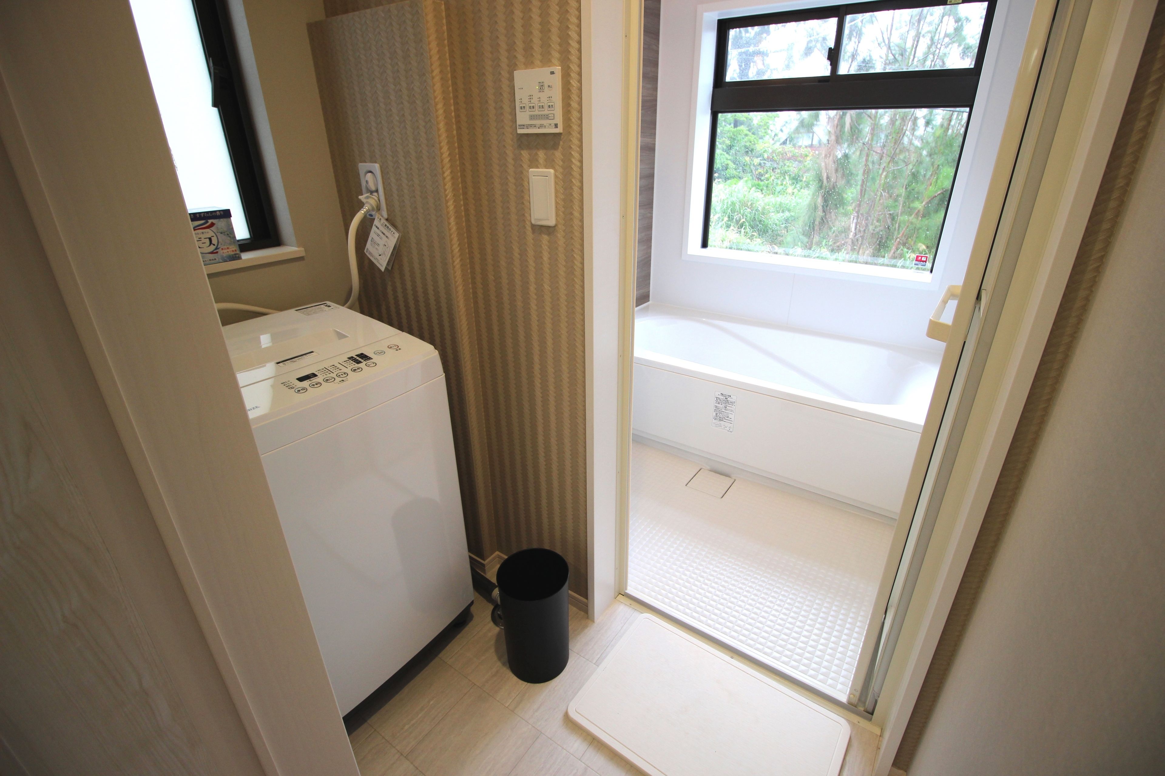 Un baño funcional con lavadora, un cesto de basura pequeño y una ventana que ofrece vistas a zonas verdes.