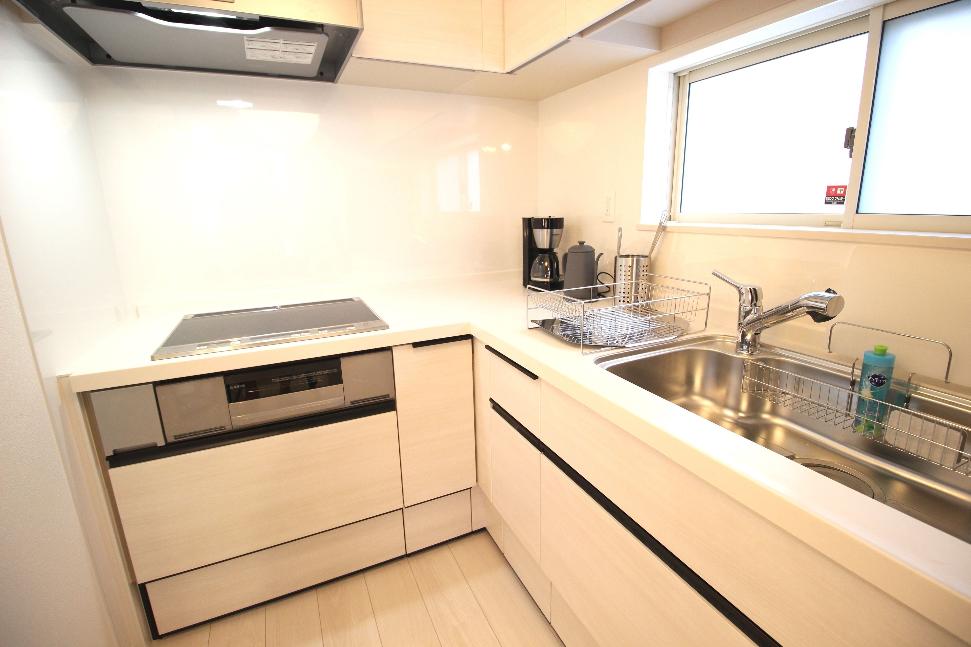 A modern kitchen with a dishwasher, a coffee maker, and a sink with a window above.