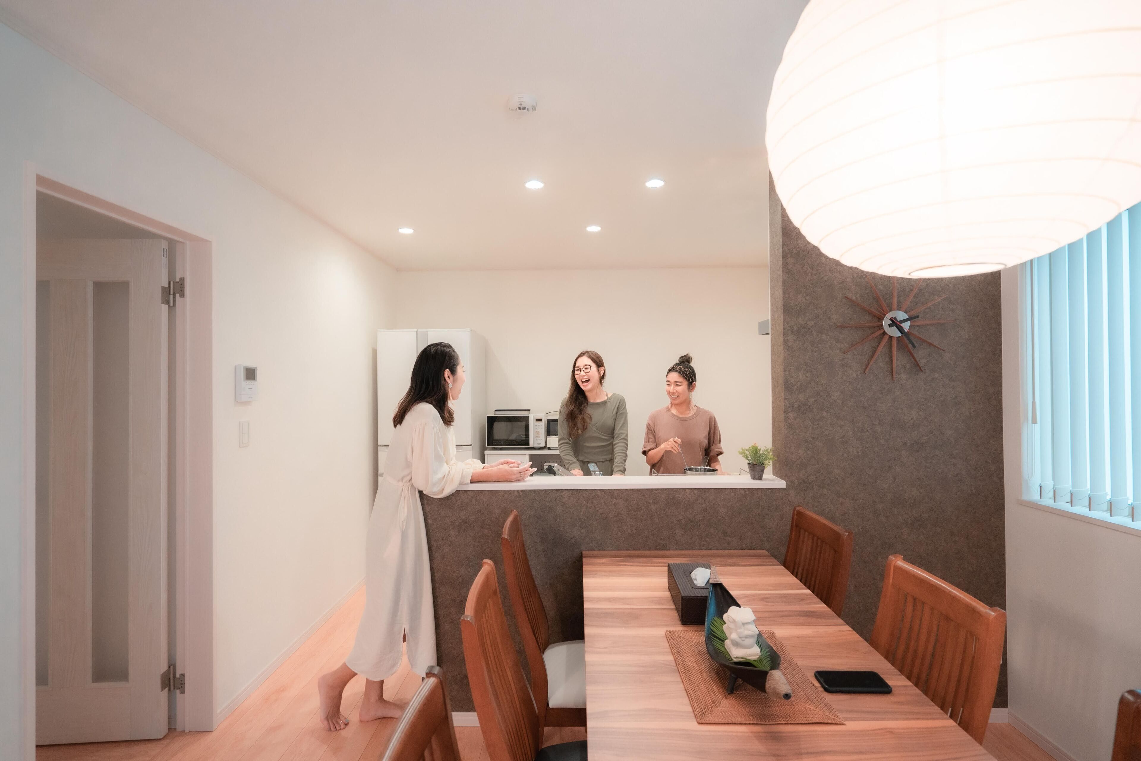 A modern dining area with a wooden table and chairs, a kitchen counter with a microwave, and a decorative wall clock.
