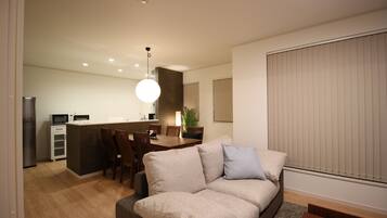 A modern living room with a sofa, a dining area with a table and chairs, and a kitchen area with appliances.