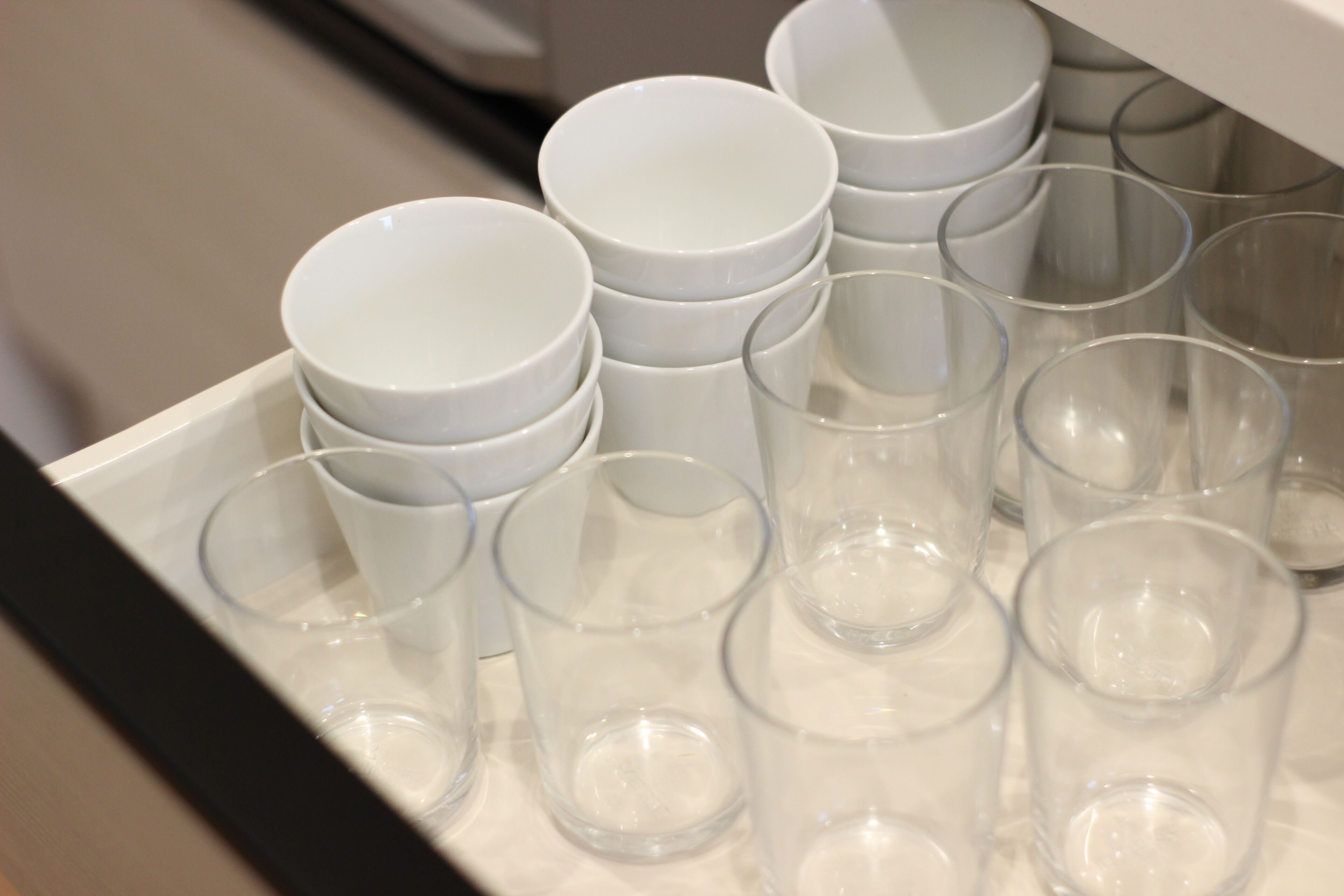 Un tiroir contenant plusieurs verres à boire transparents et des bols blancs.