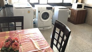 A room with a washing machine, a microwave, and a table with a floral tablecloth.