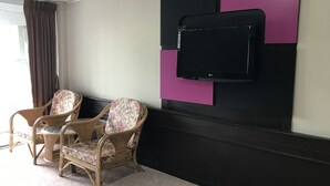 A room with two wicker chairs, a flat-screen TV mounted on a wall, and a window with curtains.