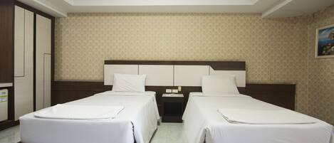 Una habitación de hotel con dos camas individuales, un cabecero de madera, una mesita de noche y un armario.
