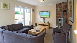 Ein Wohnzimmer mit grauem Sofa, einem Holztisch, einem an der Wand montierten Fernseher und einem Kamin.