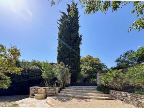 Una escalera de piedra conduce a una verja, rodeada de follaje y un árbol alto.