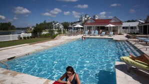 Ein Pool mit Liegestühlen und Sonnenschirmen, umgeben von Häusern und einem See.