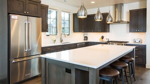 A modern kitchen with dark cabinets, stainless steel appliances, and a large island with bar stools. - SUNNY VACAY ~ 24-hr staff ~ south views ~ BBQ ~ 🐶 ~ hot tub ~ Bend  (Bend)