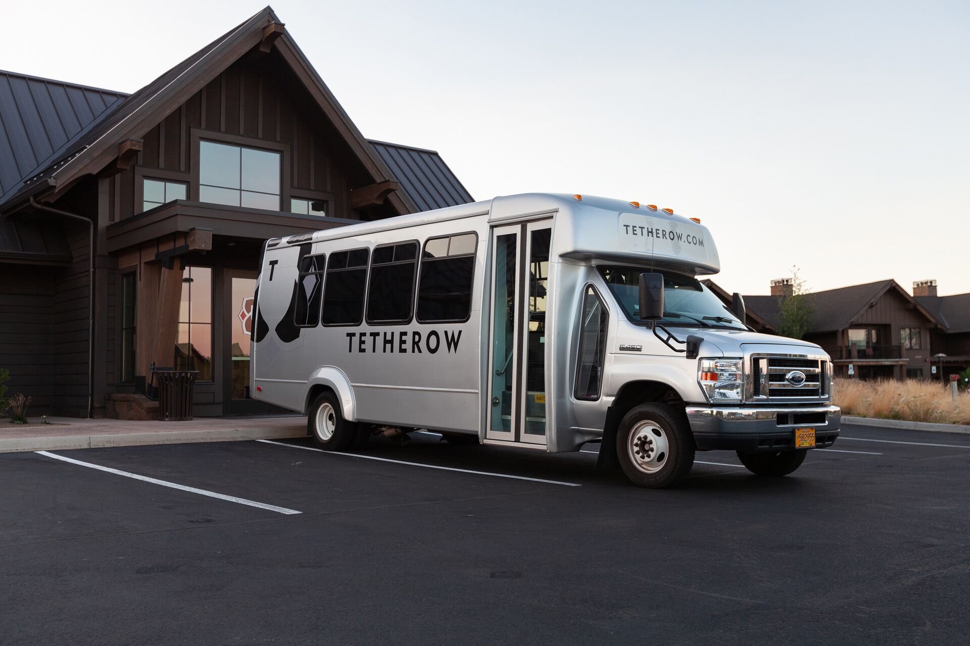 A Tetherow bus parked in front of a building with a sloped roof and large windows.