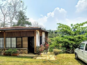 Ein Haus mit einem Ziegeldach, einer Holztür und einem Garten mit Kübelpflanzen und Rasen.
