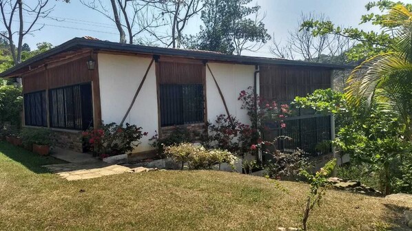 Einbungalow mit geneigtem Dach, einer Veranda und einem kleinen Vorgarten mit Rasen und Topfpflanzen.
