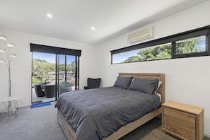 Une chambre moderne avec un grand lit, une table de chevet en bois et une vue sur la verdure par la fenêtre.