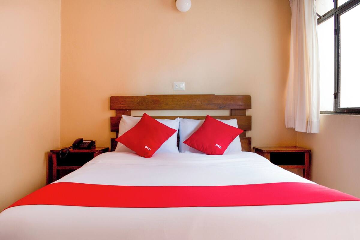Una habitación de hotel con una cama grande, dos mesitas de noche, un cabecero de madera y una ventana con cortinas.