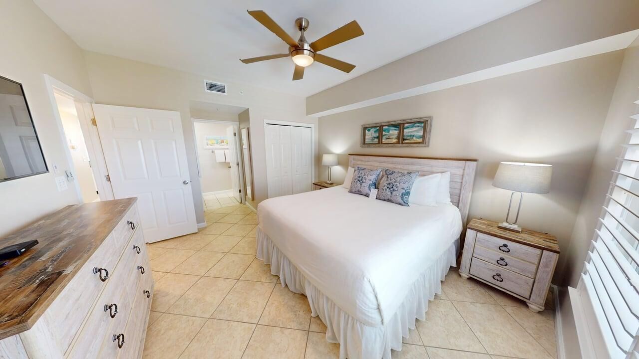 A bedroom with a bed, a nightstand, a dresser, a ceiling fan, and a door leading to another room.