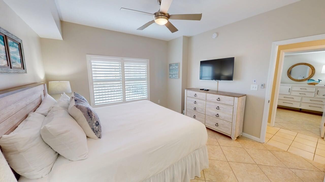 A bedroom with a bed, a dresser, a television, and a ceiling fan.