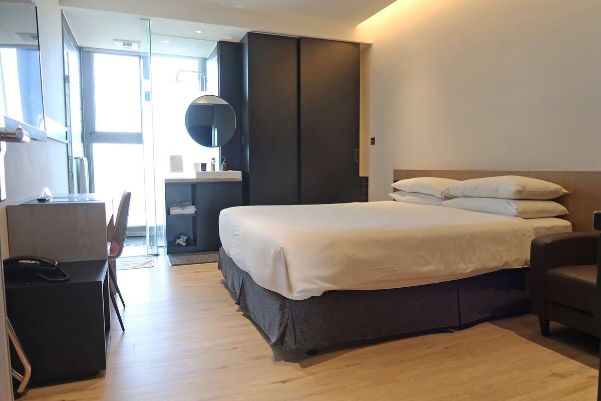 Una habitación de hotel moderna con cama, escritorio, silla y un espejo grande.