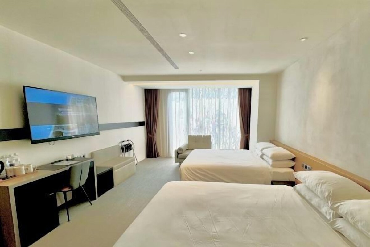 A hotel room with a bed, a desk, a chair, a TV, and a window with curtains.