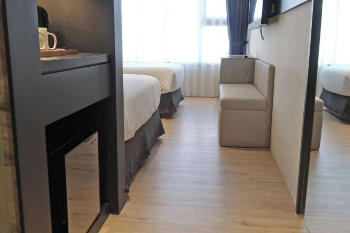 A narrow hallway with two beds and a seating area, wooden flooring, and a television on the wall.