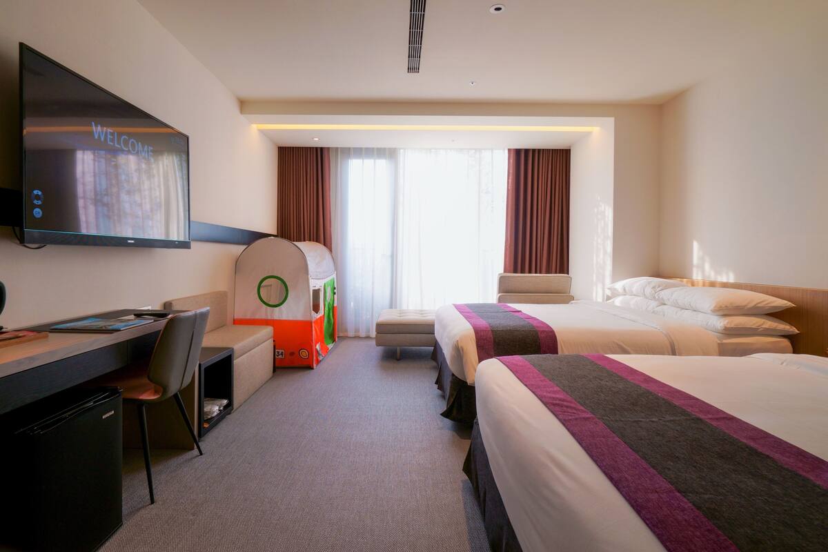 Una habitación de hotel con una cama, un escritorio, un televisor y una tienda de campaña infantil.