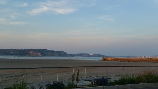 Une vue sur la côte, avec une plage, une clôture et des collines au loin.