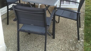 Une terrasse extérieure avec une table et quatre chaises, un canapé et un luminaire fixé au mur.