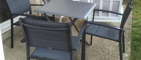 Een terras buiten met een tafel en vier stoelen, een bank, en een wandlamp.