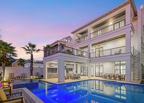 A modern multi-story house with a swimming pool, outdoor seating, and a balcony with railings. - Oasis at Park Row|Easy Beach Access|Large Private Pool|Golf Cart (Destin)