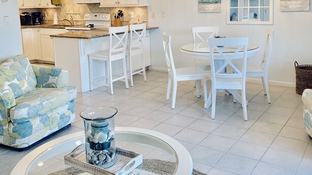 A modern kitchen with white cabinets, a dining area with white chairs, and a round coffee table with decorative items. - Steps to 30A & beach with all the comfort of home including a washer & dryer!  (Santa Rosa Beach)