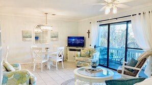 A spacious living area with a dining table, white chairs, a sofa, and a TV. - Steps to 30A & beach with all the comfort of home including a washer & dryer!  (Santa Rosa Beach)