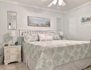 A bedroom with a bed, bedside tables, a nightstand, a ceiling fan, and a painting on the wall.