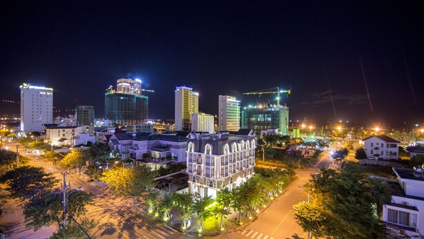 A nighttime cityscape with illuminated buildings, a prominent historic building with a balcony, and a well-lit street with trees. - Hong Chau Hotel (Da Nang)