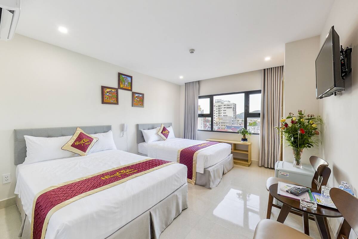 A hotel room with two beds, a desk with a chair, a TV, and a window with a city view.